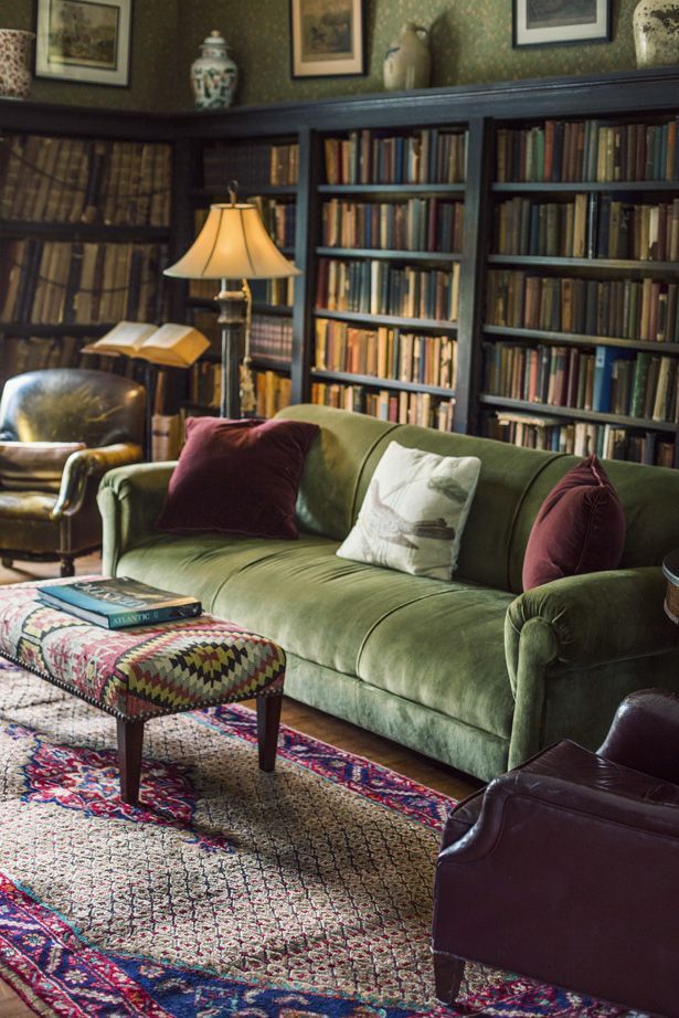 Lived in library with plush green sofa, leather side chairs, green wallpaper, bookshelves, patterned ottoman and rug.