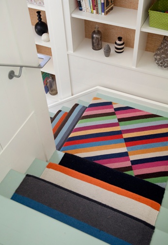 Painted stairs with a colorful striped carpet runner. Built in storage and shelving unit