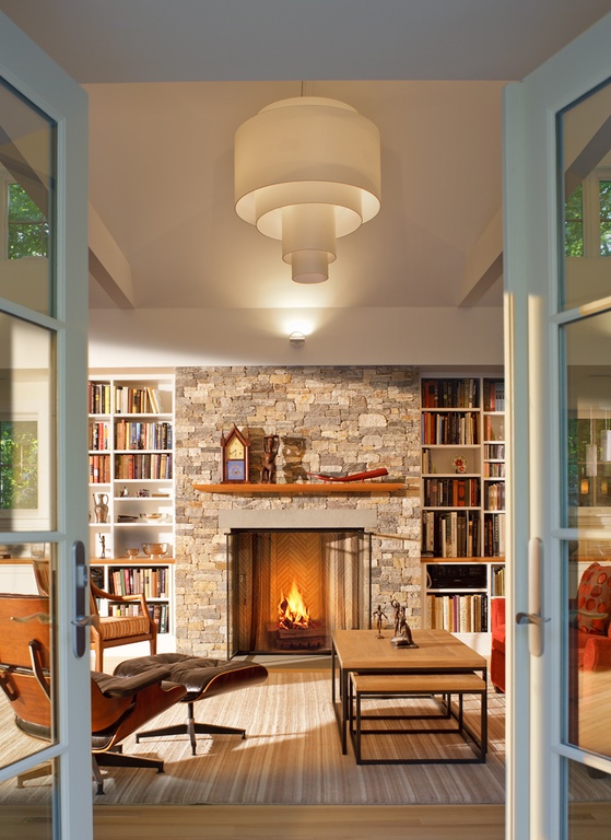 Rustic living room with stone fireplace, stripped area rug, wooden coffee table, bookshelves, and brown recliner