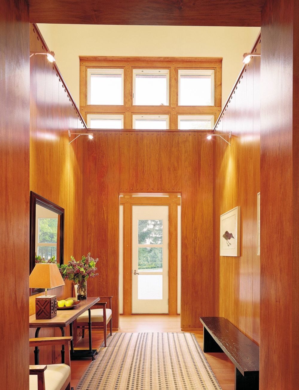 The double height hall of a New Jersey home is grounded by an interior room paneled in yellow cypress