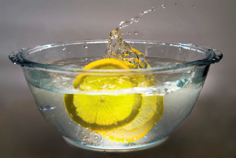 two lemon slices falling into bowl with water on a grey background