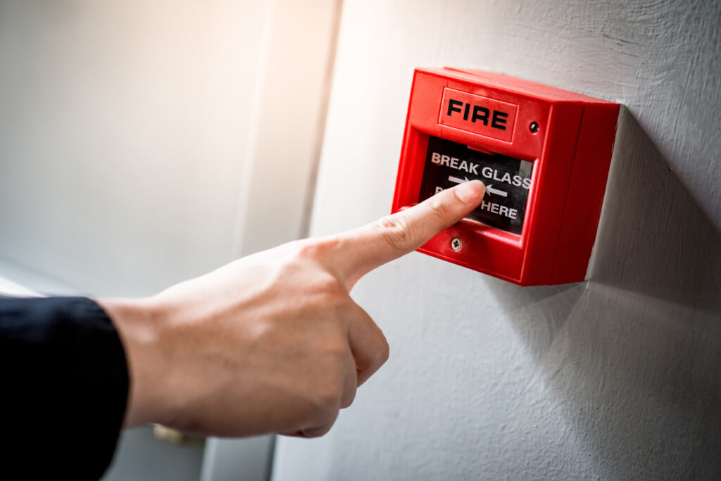 Male hand pointing at red fire alarm switch