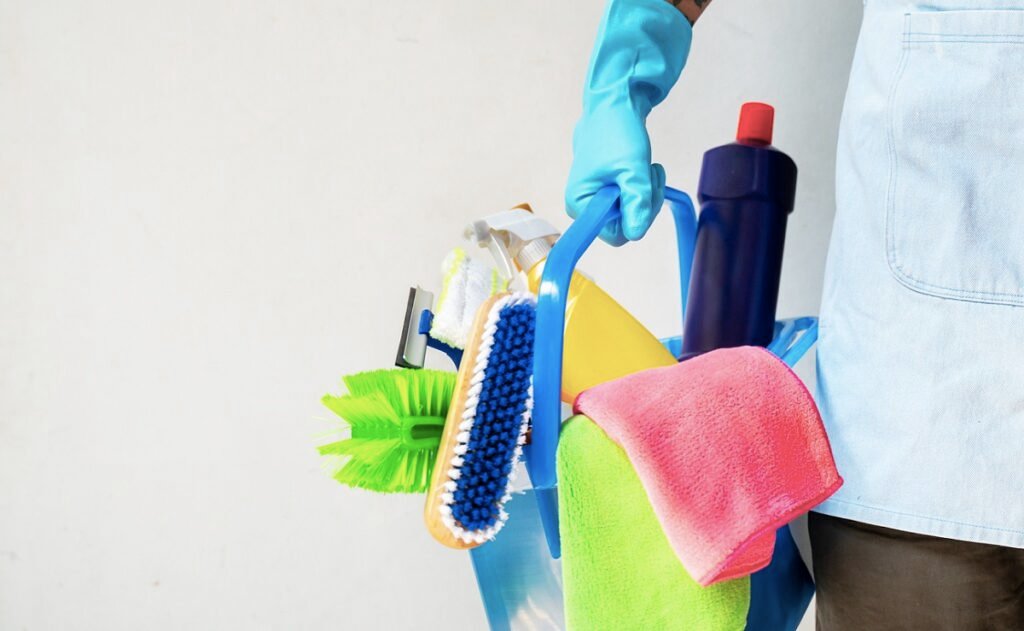 Man holding mop and plastic bucket with brushes, gloves and detergents in the kitchen