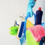 Man holding mop and plastic bucket with brushes, gloves and detergents in the kitchen